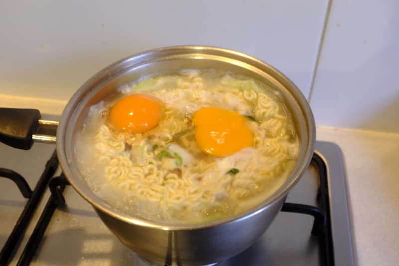 Ramen being cooked with eggs cracked on top